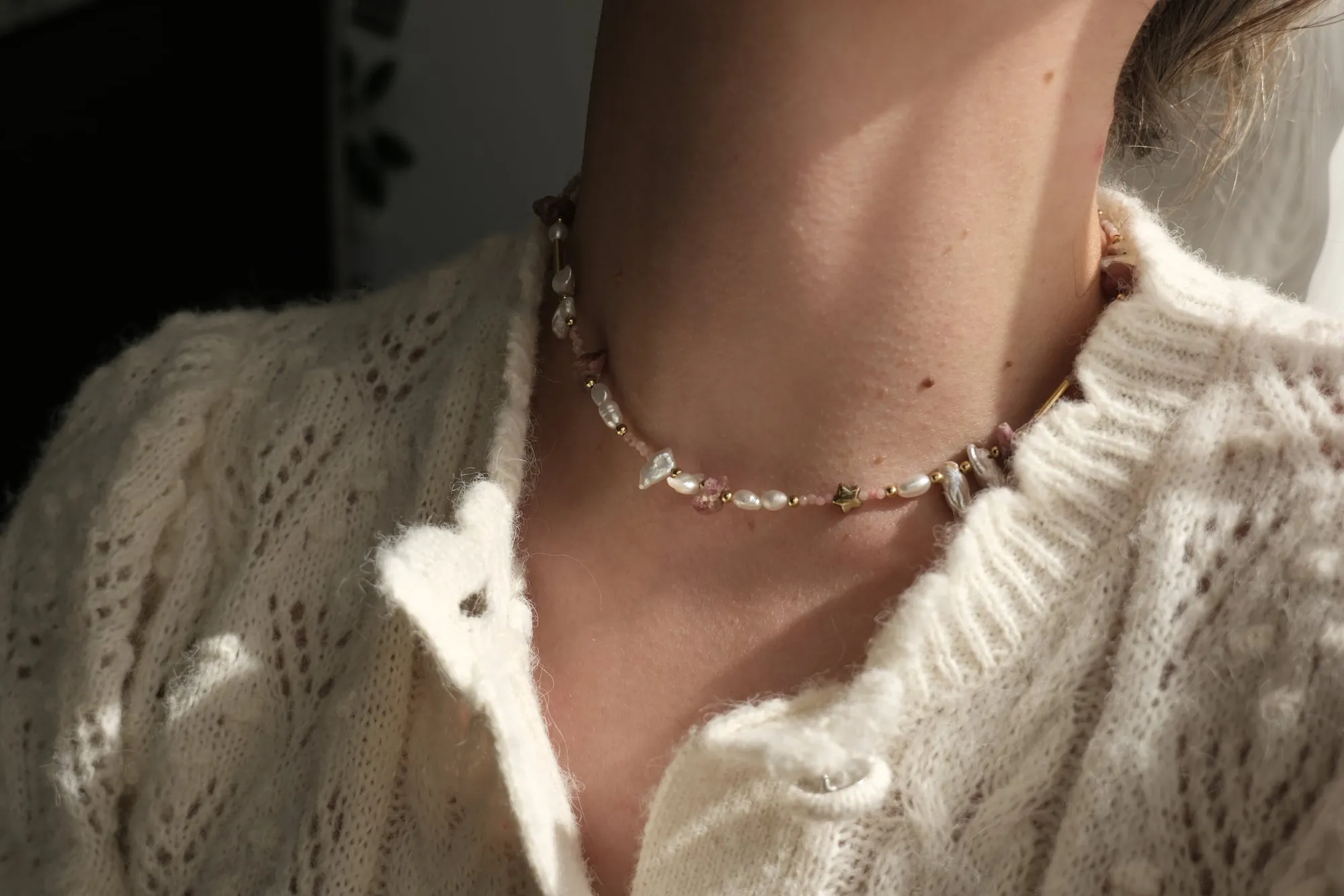The Blush necklace worn over a cream cardigan — rose stones, baroque pearls and a gold star